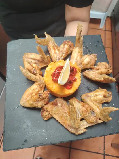 Alitas de pollo fritas alrededor de un tomate relleno, sobre una pizarra