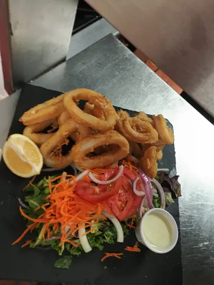 Ración de calamares fritos con limón y ensalada sobre una pizarra