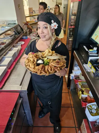 Una cocinera sonriente sale de la cocina con una fuente de fritura de pescado