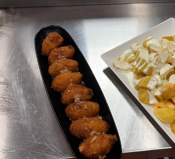 Una fuente alargada de croquetas, con patatas bravas al lado