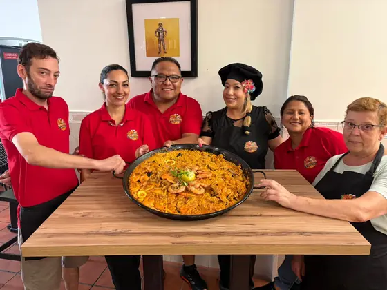 El equipo del bar, con polos rojos, alrededor de una paella grande en una mesa del salón