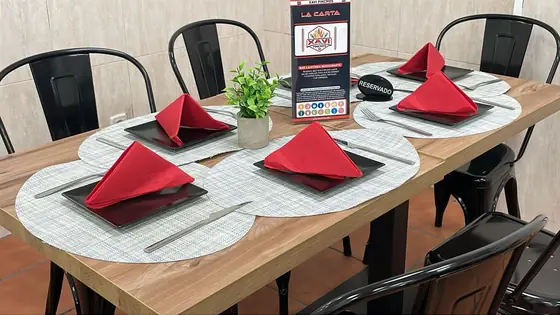 Mesa del salón preparada, con servilletas rojas, platos negros y el cartel de reservado