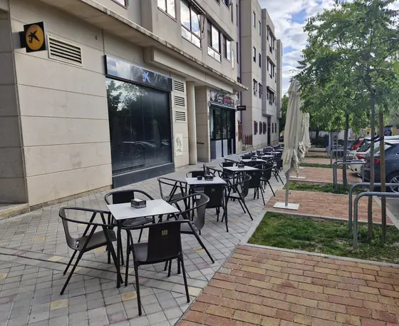 La terraza del bar en la calle Asturias, con mesas y sillas negras, sombrillas y árboles en la acera