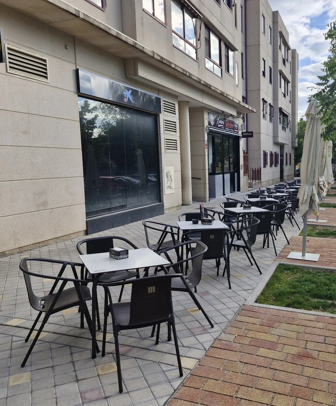 La terraza del bar en la calle Asturias, con mesas y sillas negras, sombrillas y árboles en la acera