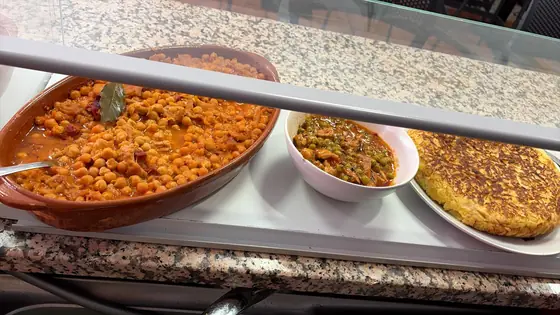 Cazuela de garbanzos, un cuenco de guiso y una tortilla de patatas en la vitrina